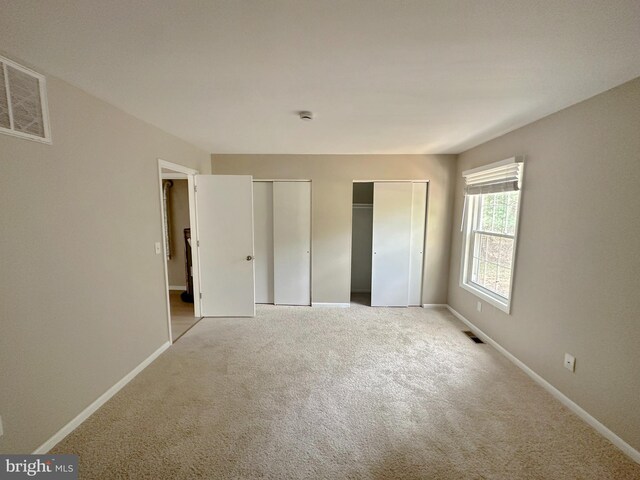 unfurnished bedroom with multiple closets, baseboards, and light carpet