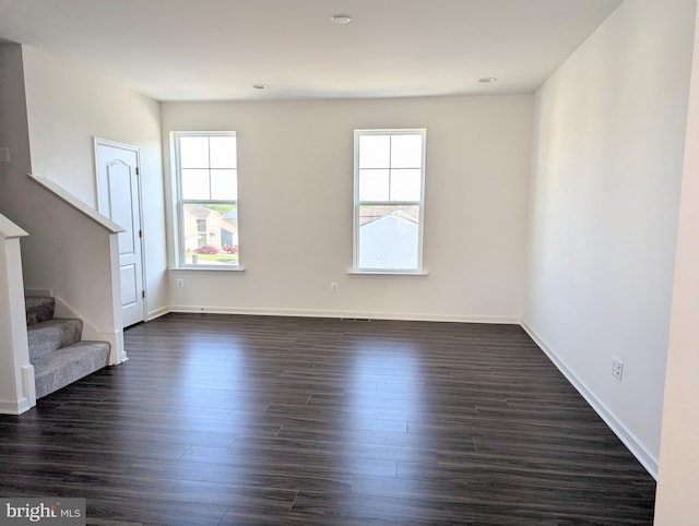unfurnished living room with stairs, dark wood-type flooring, and baseboards