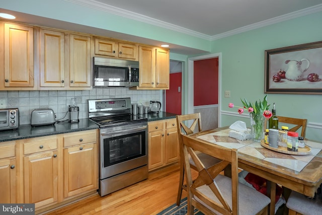 kitchen with stainless steel appliances, ornamental molding, light wood-style flooring, dark countertops, and a wainscoted wall