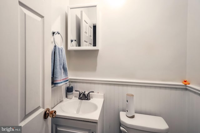 bathroom featuring a wainscoted wall, toilet, and vanity