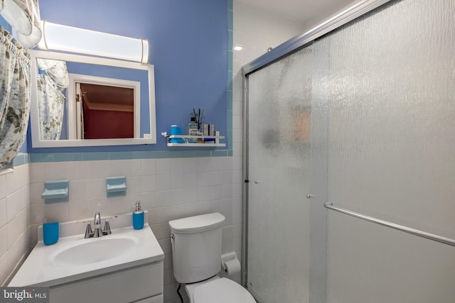 full bath with tile walls, a shower stall, vanity, toilet, and wainscoting