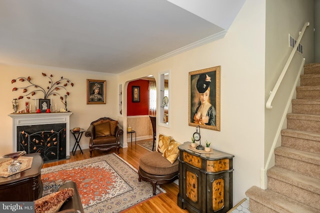 living room featuring arched walkways, wood finished floors, stairs, ornamental molding, and a fireplace