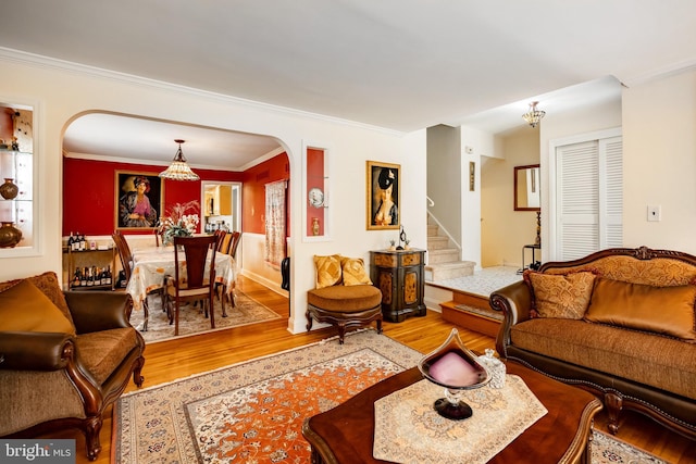 living area with arched walkways, wood finished floors, stairs, crown molding, and a chandelier