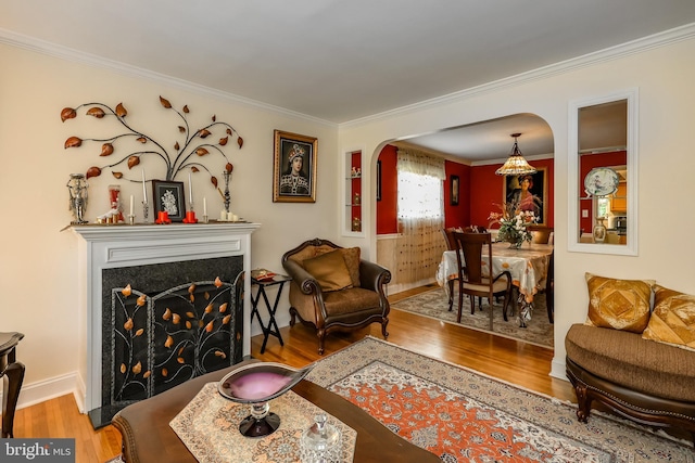 living room with wood finished floors, arched walkways, crown molding, a fireplace with flush hearth, and baseboards