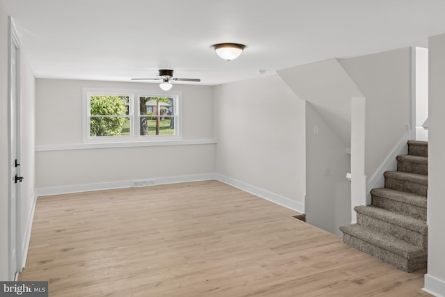 empty room featuring light wood finished floors, stairs, a ceiling fan, and baseboards