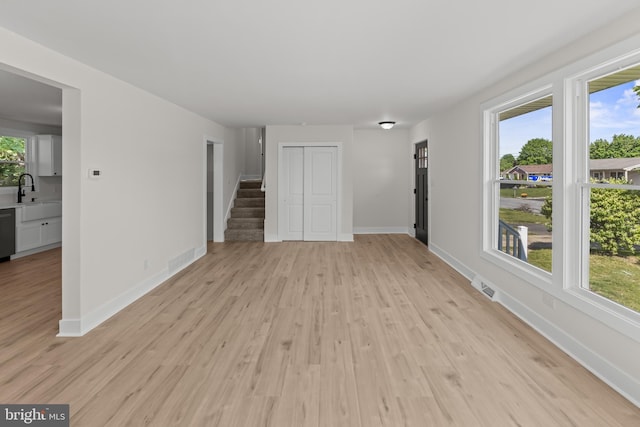 unfurnished living room with light wood-type flooring, stairs, and baseboards