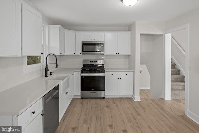 kitchen with appliances with stainless steel finishes, a sink, decorative backsplash, and white cabinetry