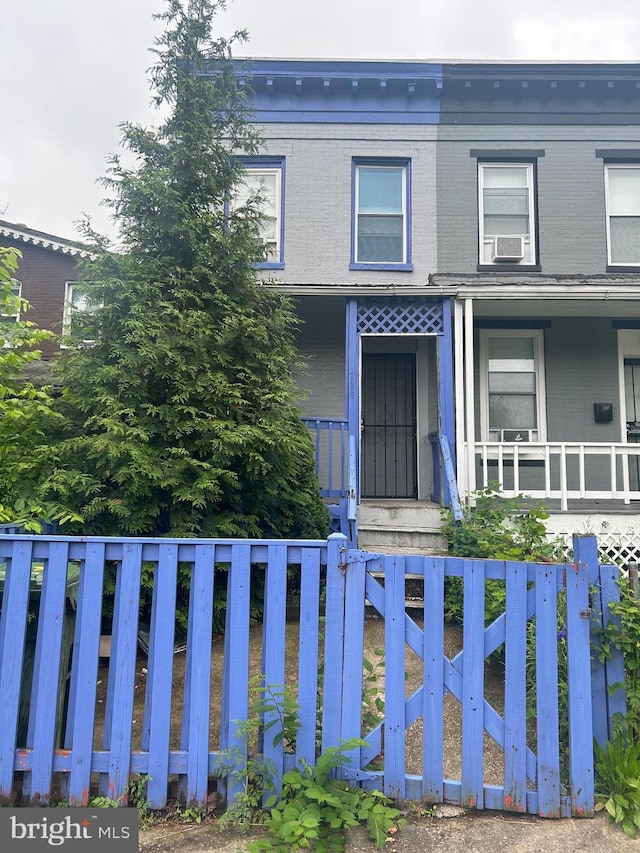 2859 W Lanvale St, Baltimore, MD 21216 - view of front of house with covered porch, a fenced front yard, brick siding, cooling unit, and a gate