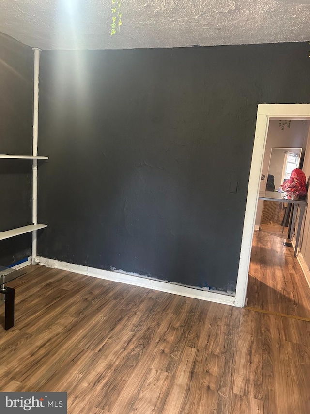 unfurnished room featuring wood finished floors, a textured ceiling, and baseboards
