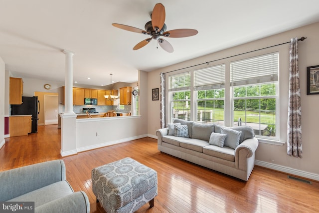 living area featuring ornate columns, ceiling fan, light wood-type flooring, and baseboards