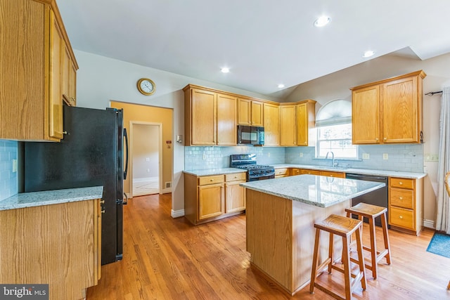 kitchen with black appliances, a breakfast bar area, a sink, light wood-style floors, and lofted ceiling