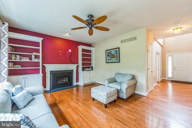 living room featuring wood finished floors, ceiling fan, a fireplace, and baseboards