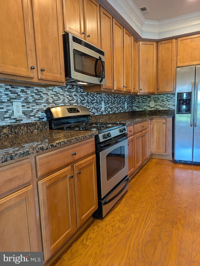 kitchen featuring appliances with stainless steel finishes, dark stone counters, tasteful backsplash, brown cabinets, and ornamental molding