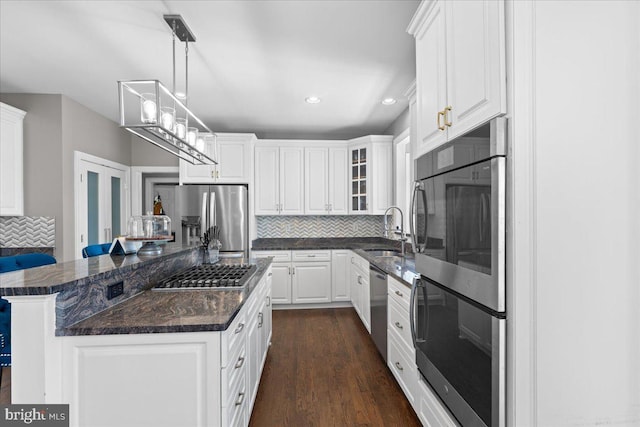 kitchen featuring stainless steel appliances, a sink, backsplash, white cabinets, and a center island