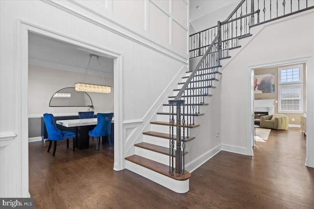 stairway with wood finished floors, crown molding, a fireplace, baseboards, and a towering ceiling