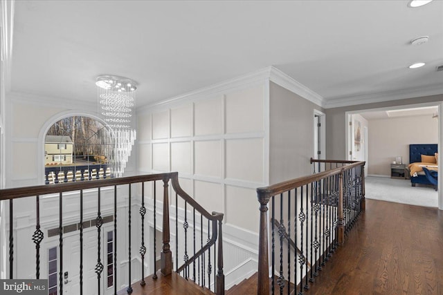 hall featuring an upstairs landing, a decorative wall, a chandelier, wood finished floors, and crown molding