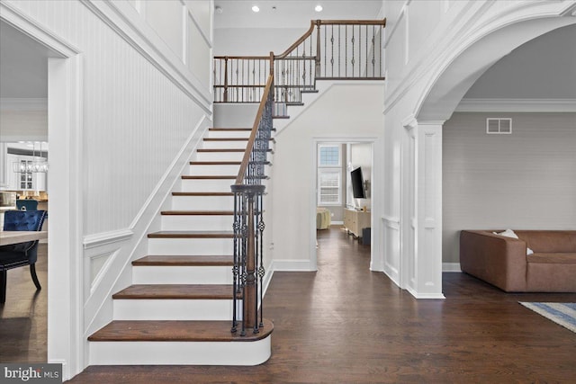 foyer featuring wood finished floors, stairs, crown molding, arched walkways, and decorative columns