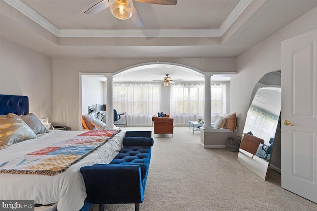 carpeted bedroom featuring decorative columns, arched walkways, a tray ceiling, crown molding, and a ceiling fan