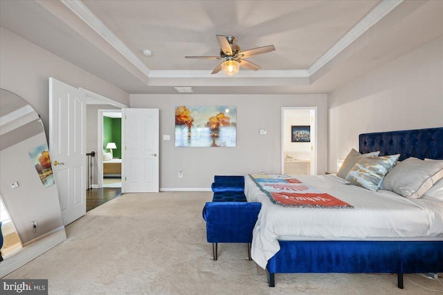 carpeted bedroom featuring a tray ceiling, baseboards, crown molding, and connected bathroom