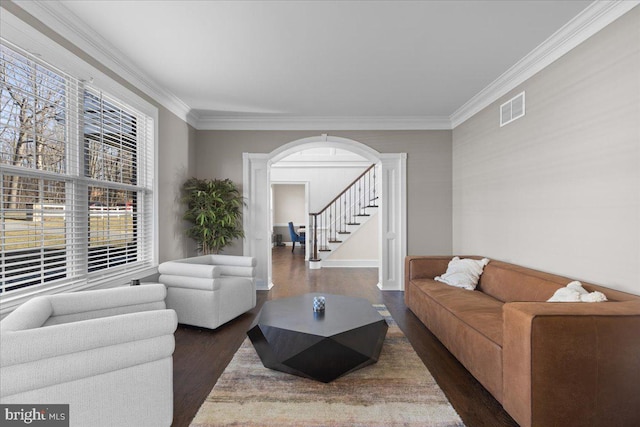 living room featuring wood finished floors, arched walkways, ornamental molding, stairway, and baseboards