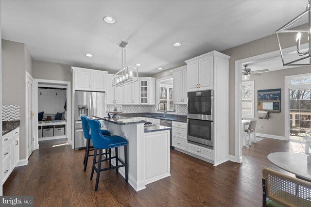 kitchen featuring stainless steel appliances, dark countertops, tasteful backsplash, white cabinetry, and recessed lighting