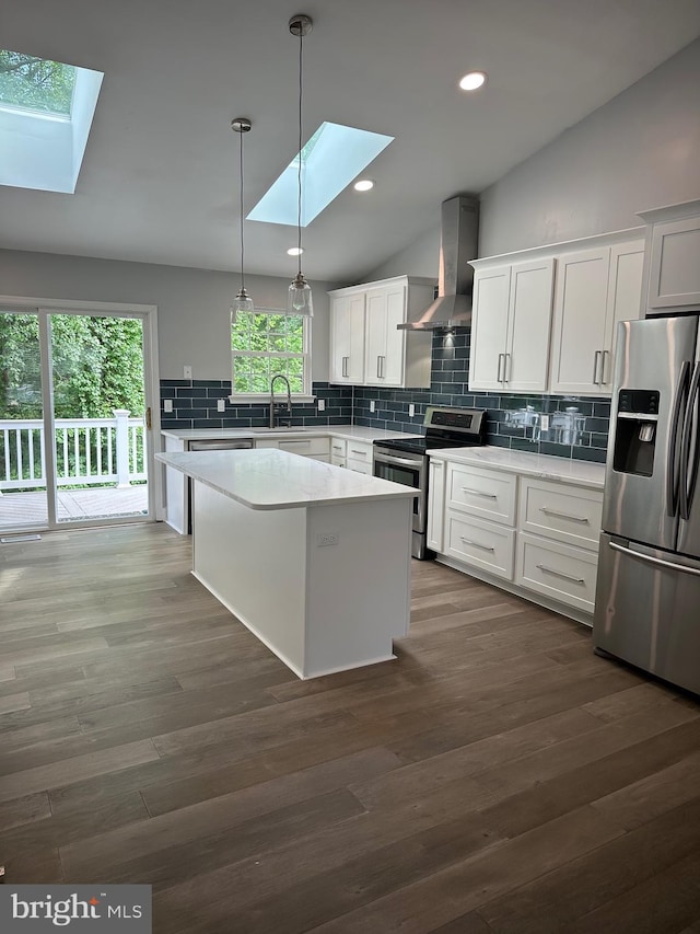 kitchen with a skylight, appliances with stainless steel finishes, wall chimney range hood, backsplash, and lofted ceiling