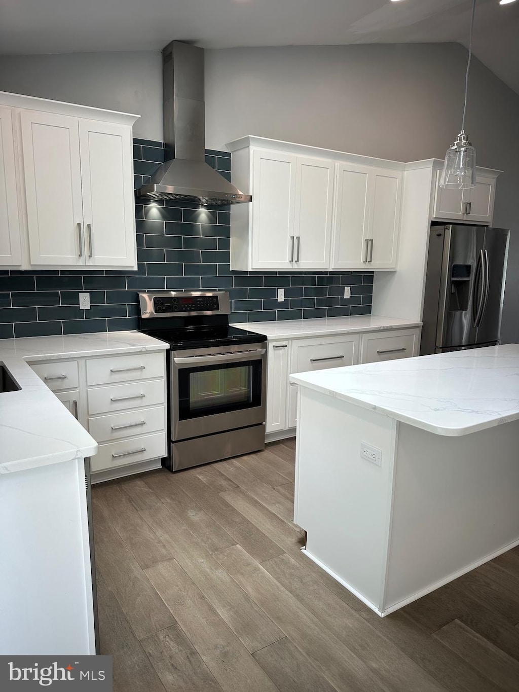 kitchen with stainless steel appliances, wall chimney range hood, vaulted ceiling, wood finished floors, and tasteful backsplash
