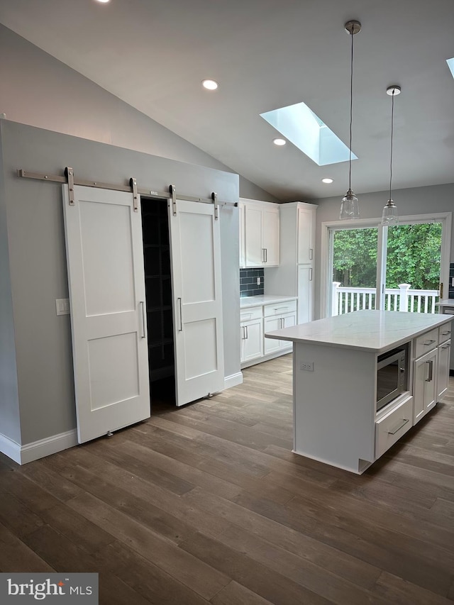 kitchen with stainless steel microwave, a skylight, vaulted ceiling, white cabinets, and a barn door