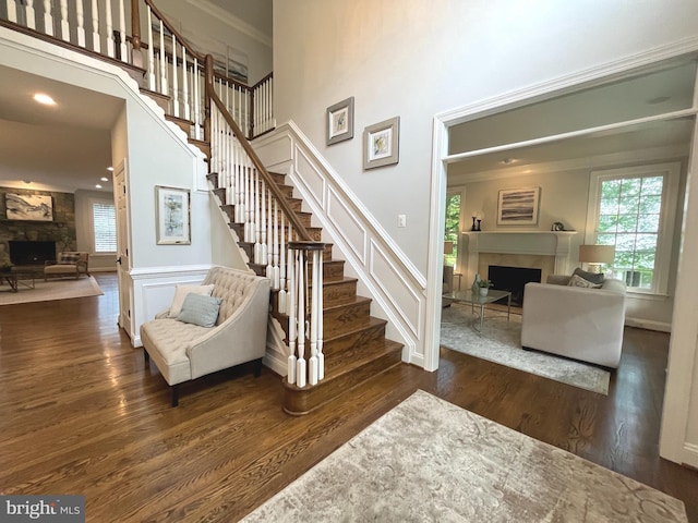 staircase featuring a fireplace, wood finished floors, a high ceiling, and baseboards