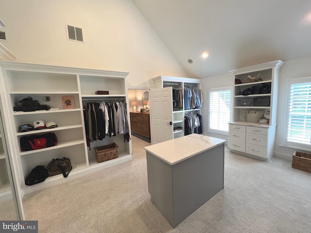 walk in closet with light carpet and high vaulted ceiling