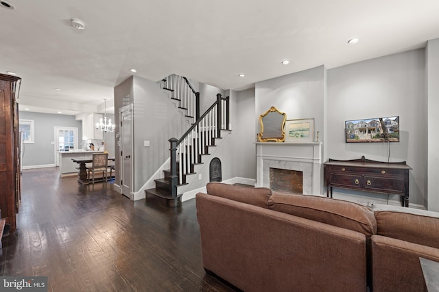 living room featuring dark wood-type flooring, stairs, a high end fireplace, a chandelier, and baseboards