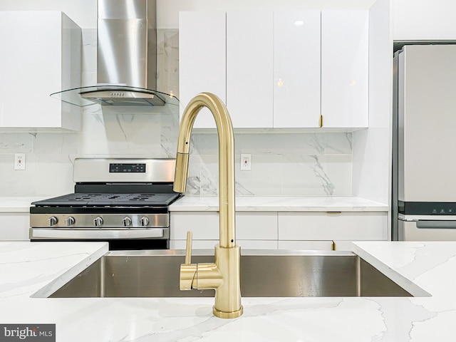 kitchen featuring fridge, wall chimney exhaust hood, stainless steel gas range oven, tasteful backsplash, and white cabinets