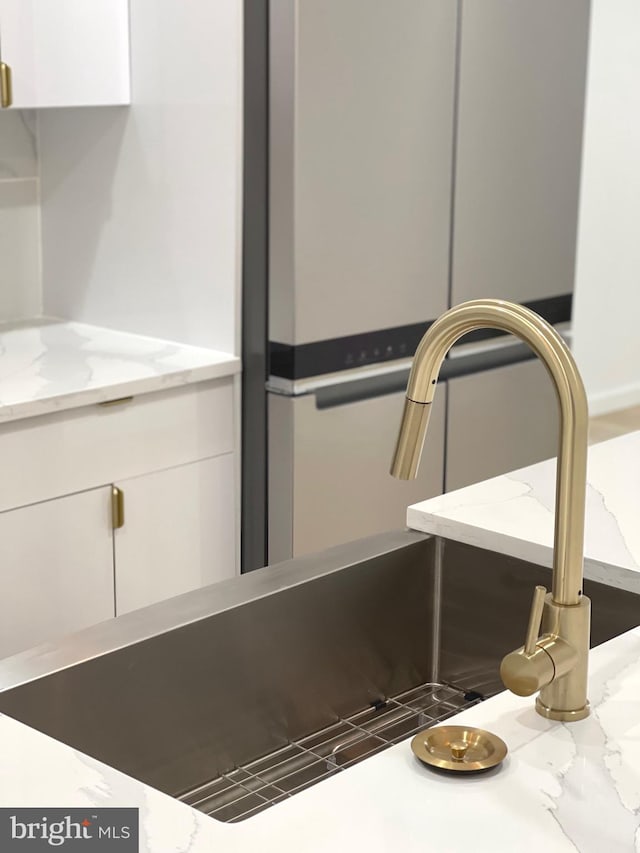 kitchen view of white cabinets, light stone countertops, and a sink