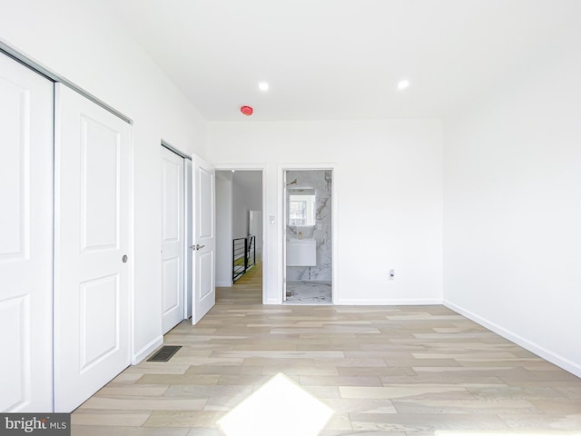 unfurnished bedroom featuring light wood-type flooring, connected bathroom, baseboards, and recessed lighting