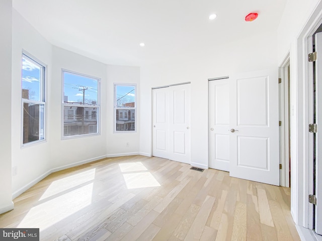 unfurnished bedroom with two closets, light wood finished floors, recessed lighting, and baseboards