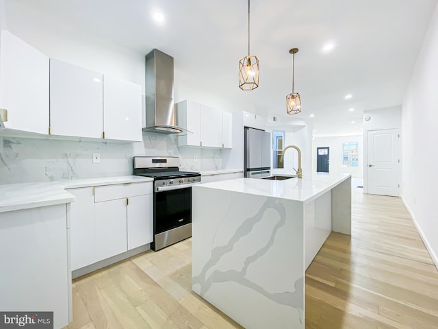 kitchen featuring stainless steel gas range oven, wall chimney exhaust hood, freestanding refrigerator, a sink, and light wood-style flooring
