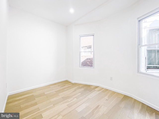 spare room featuring light wood finished floors, baseboards, and lofted ceiling