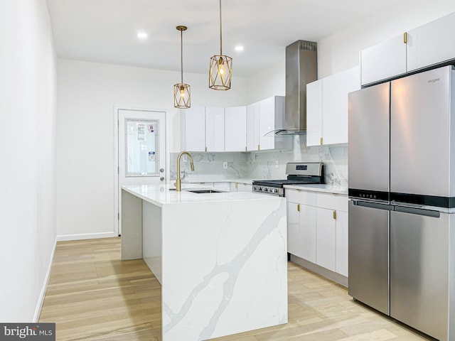 kitchen featuring appliances with stainless steel finishes, a sink, wall chimney range hood, decorative backsplash, and light wood-style flooring