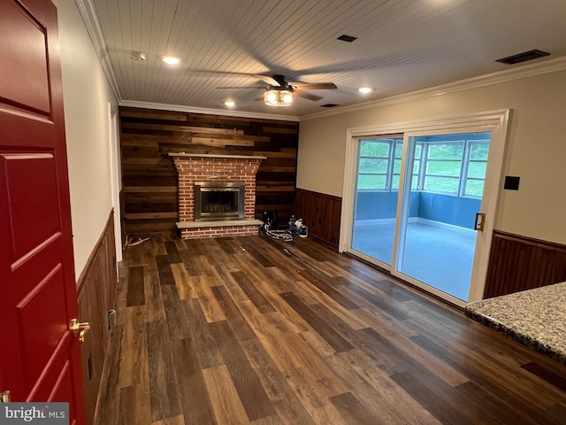 unfurnished living room with wooden walls, ceiling fan, a wainscoted wall, ornamental molding, and a fireplace