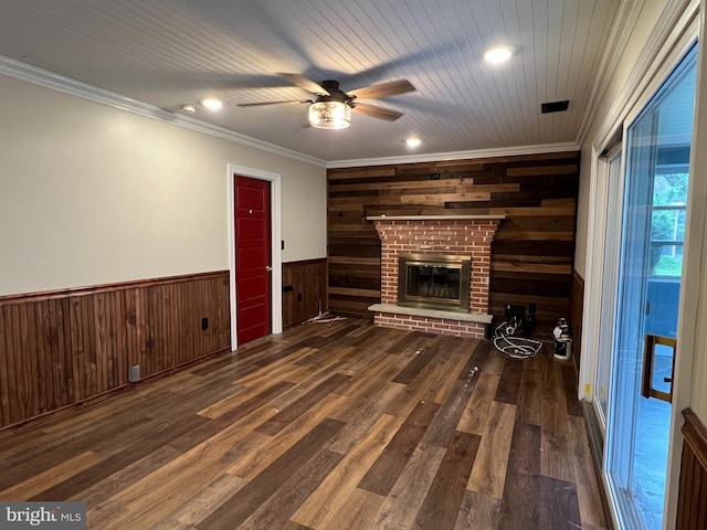 unfurnished living room with wood walls, ceiling fan, wood finished floors, wainscoting, and crown molding