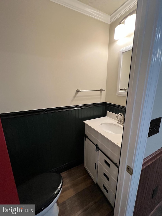 half bath featuring a wainscoted wall, crown molding, vanity, wood finished floors, and toilet