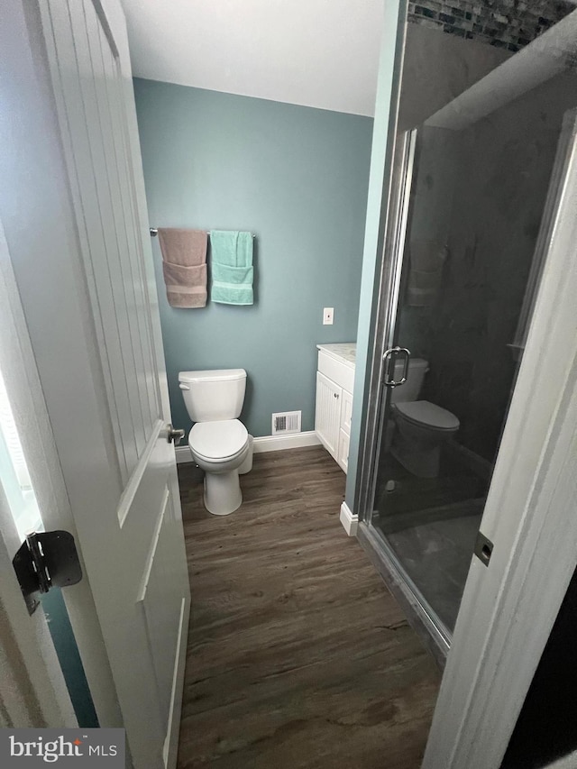 bathroom with toilet, wood finished floors, a stall shower, vanity, and baseboards