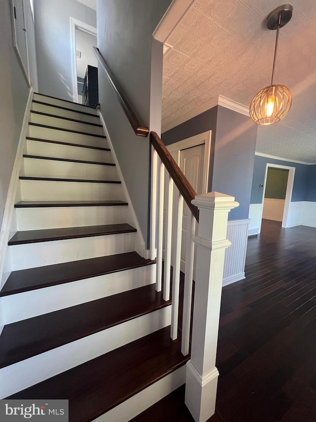 staircase with wood finished floors, an ornate ceiling, and a wainscoted wall
