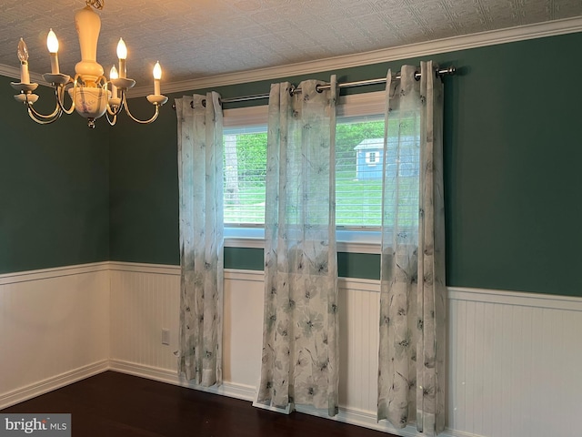 empty room featuring wainscoting, a chandelier, wood finished floors, and crown molding