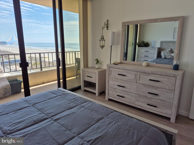 bedroom featuring access to exterior, light wood-type flooring, view of water and beach, and baseboards