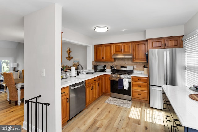 kitchen with appliances with stainless steel finishes, light countertops, light wood-type flooring, and under cabinet range hood
