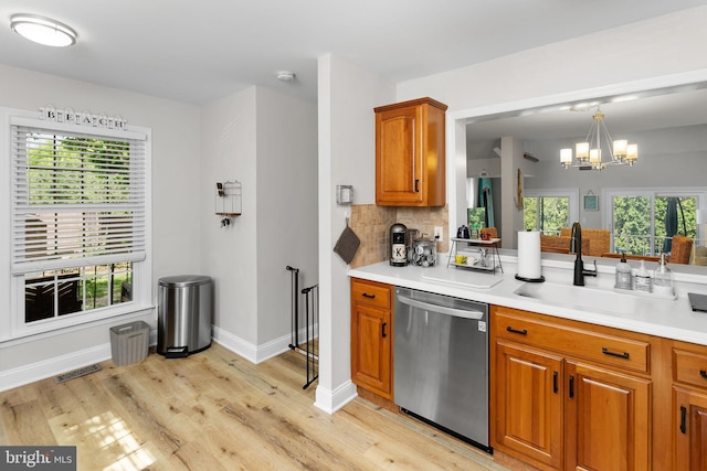 kitchen featuring stainless steel dishwasher, a chandelier, light wood-style floors, brown cabinetry, and a sink