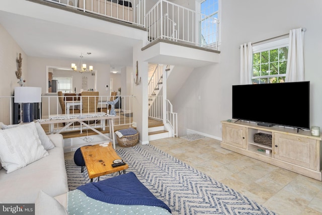 living room with stairs, a chandelier, a high ceiling, baseboards, and stone finish flooring