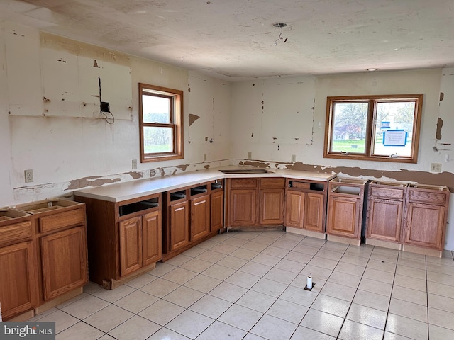 kitchen with healthy amount of natural light, light tile patterned flooring, brown cabinets, a sink, and a textured ceiling