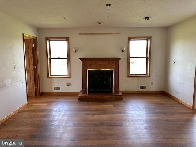 unfurnished living room with wood finished floors, healthy amount of natural light, and a fireplace with raised hearth